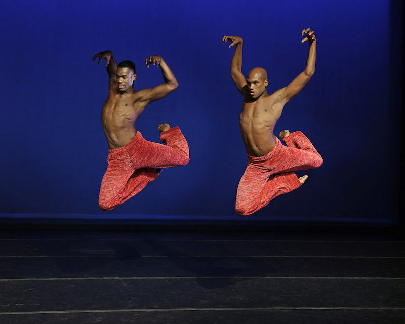 Two Ailey male dancers are in midair legs bent behind them